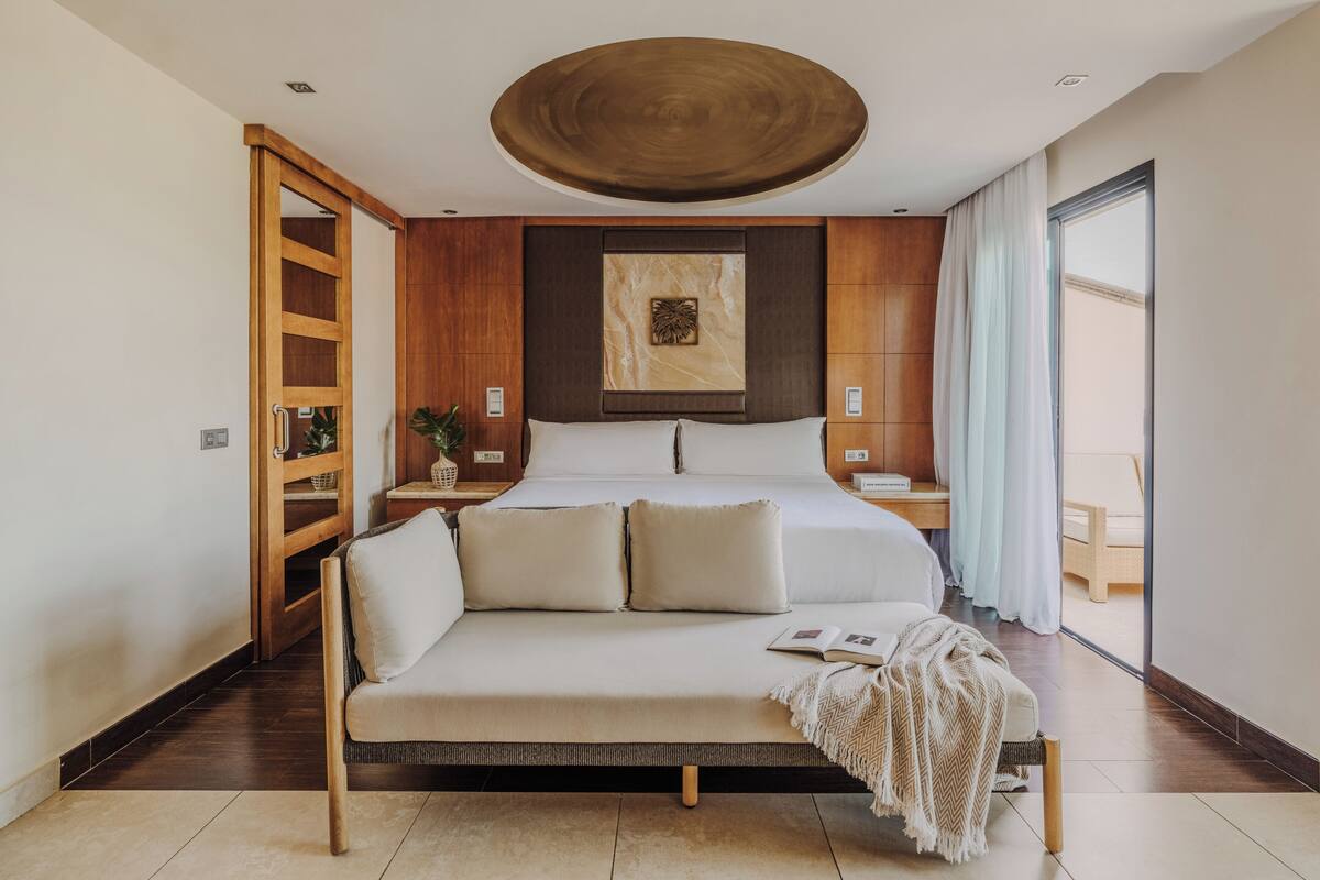 Une chambre à coucher moderne avec un lit, un canapé, une armoire en bois et un grand luminaire circulaire au plafond.
