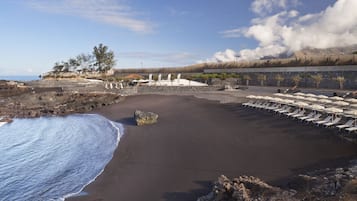 En la playa, arena negra, sillas reclinables de playa, sombrillas