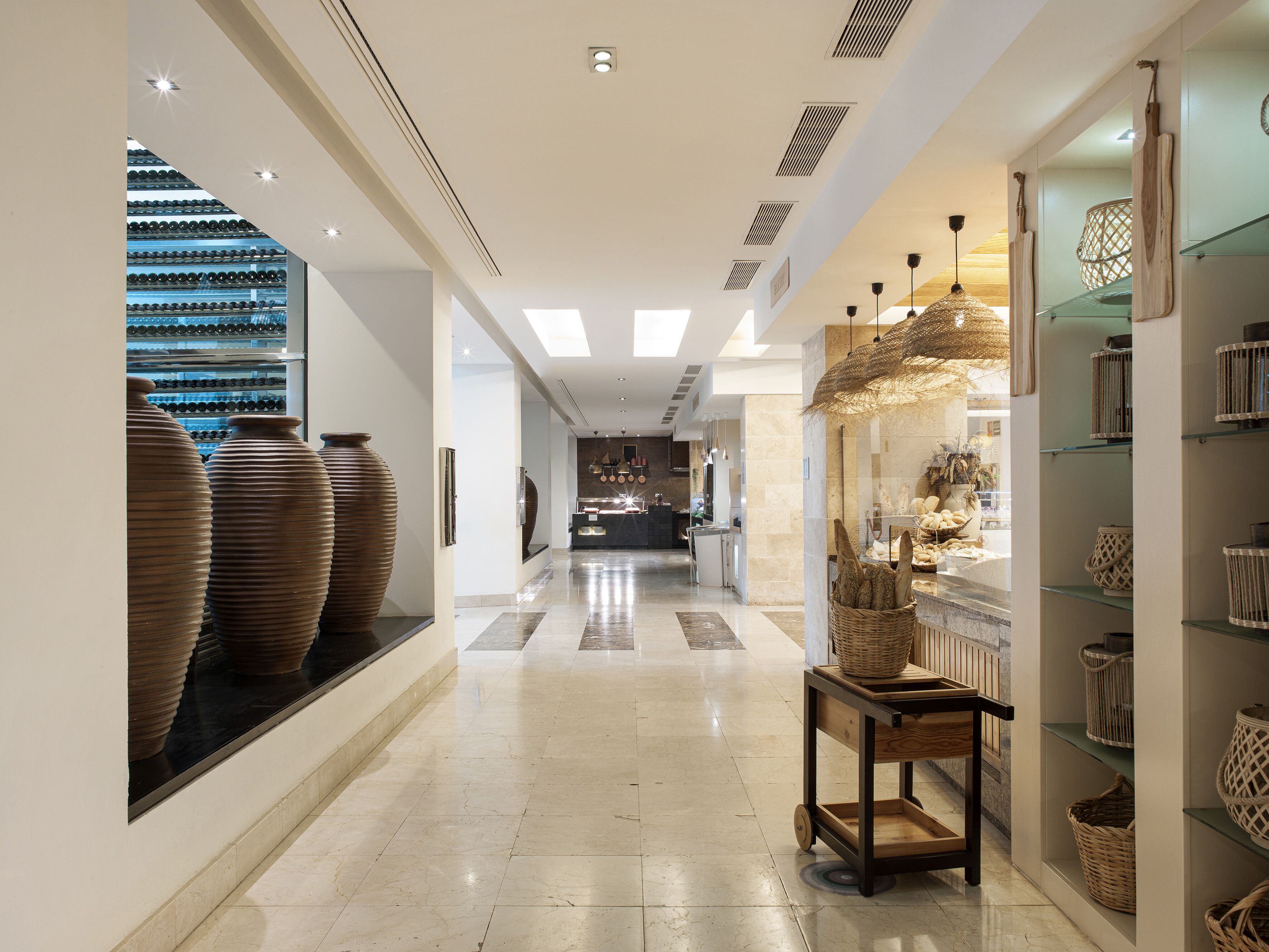 Un corredor moderno de hotel con un pasillo central, una exhibición de grandes jarrones a la izquierda y una variedad de cestas y recipientes a la derecha.