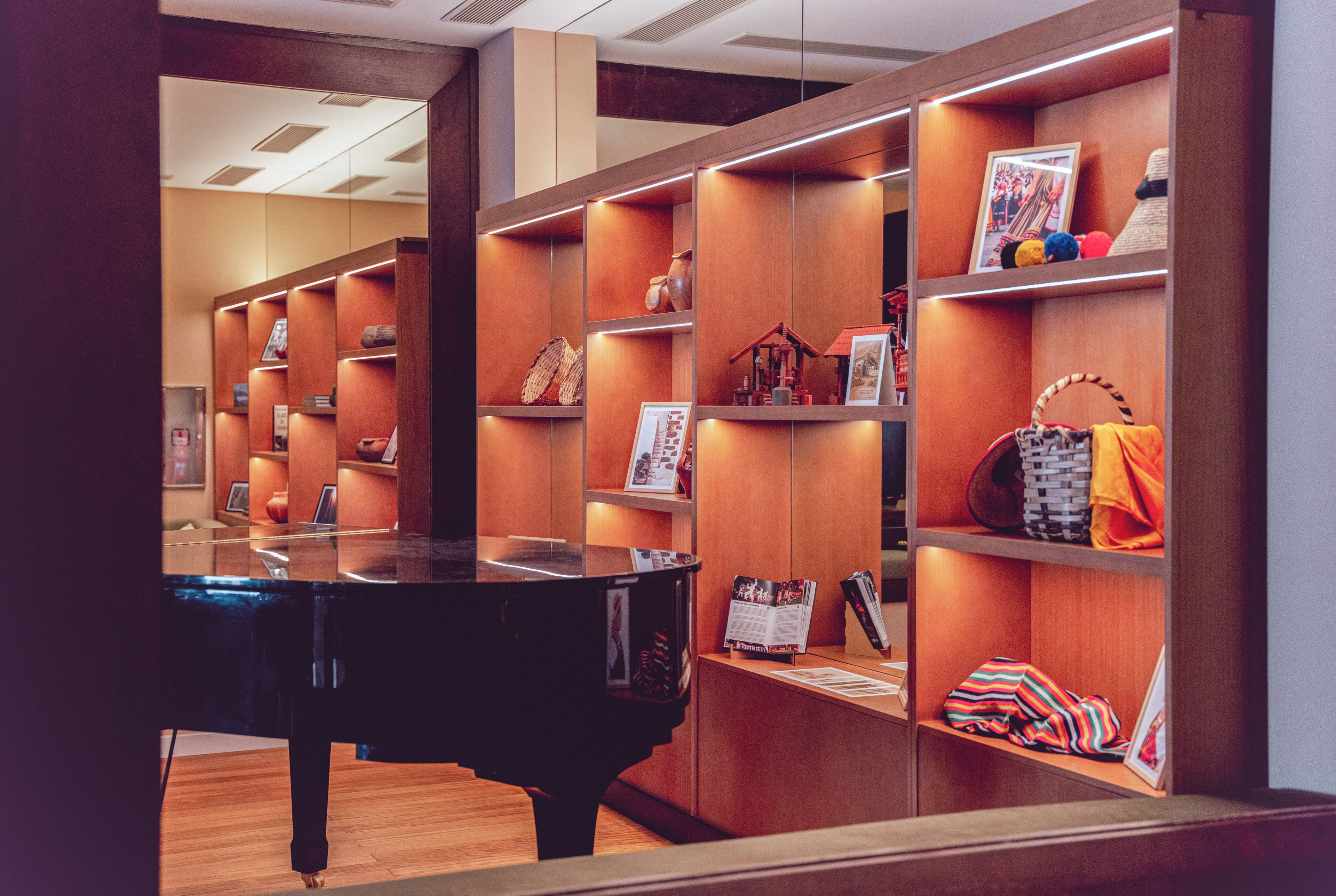 A room with a grand piano, wooden shelving with various items, and a polished wooden floor.