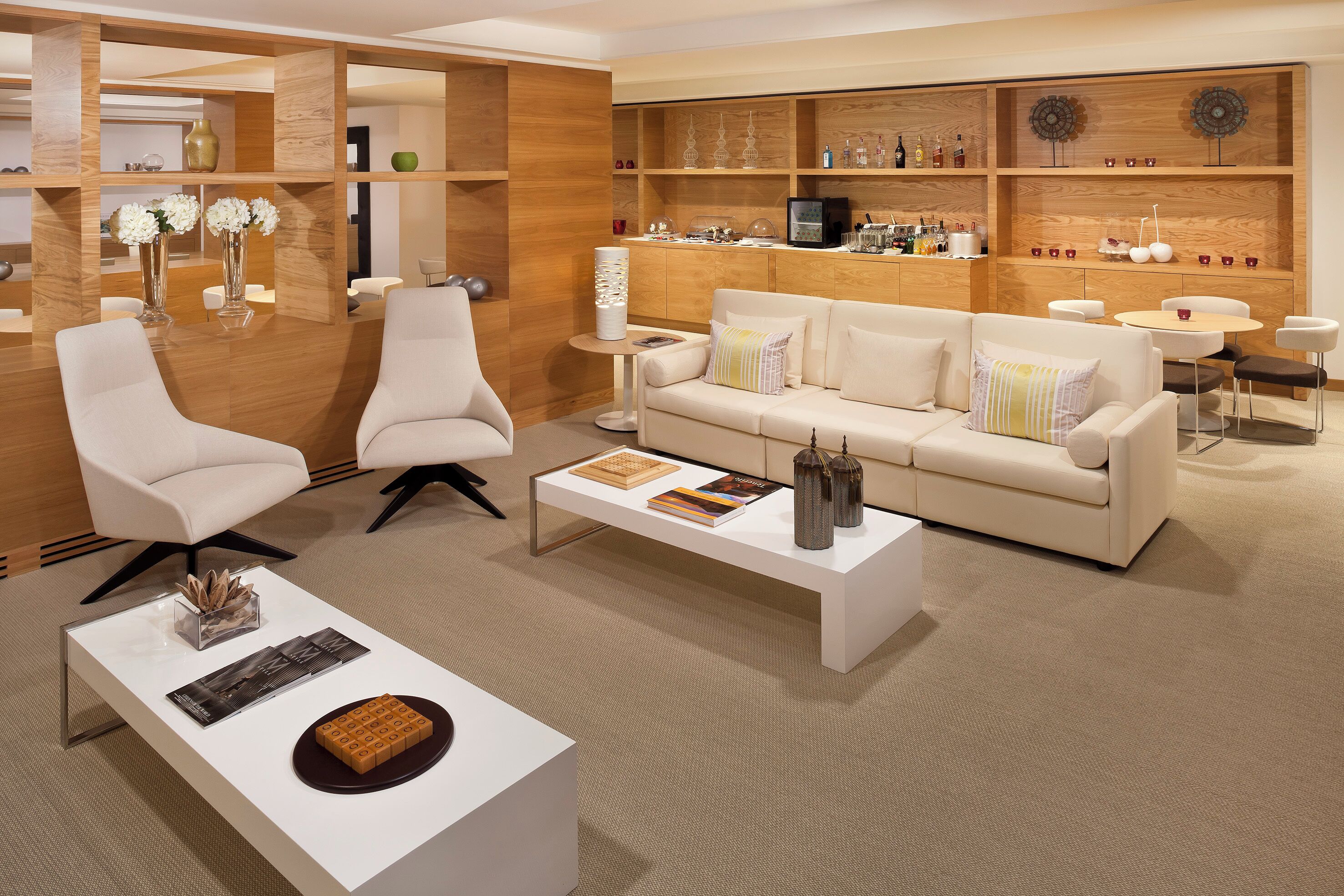 Una sala de estar moderna con un sofá blanco, dos sillones blancos, una mesita de centro y una estantería de madera con objetos decorativos.