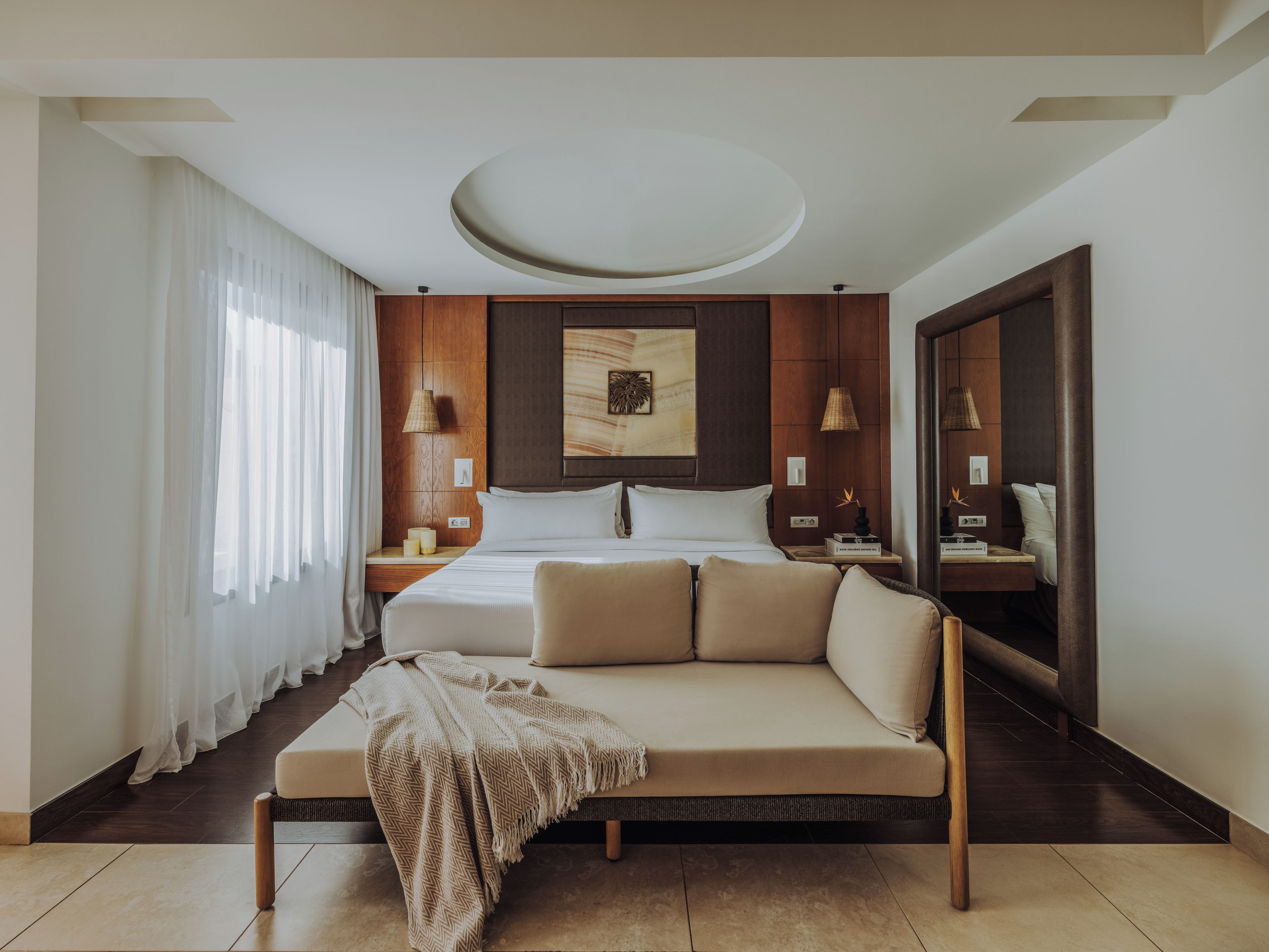 A modern hotel room with a large bed, a sofa, a mirror, and a ceiling light fixture.