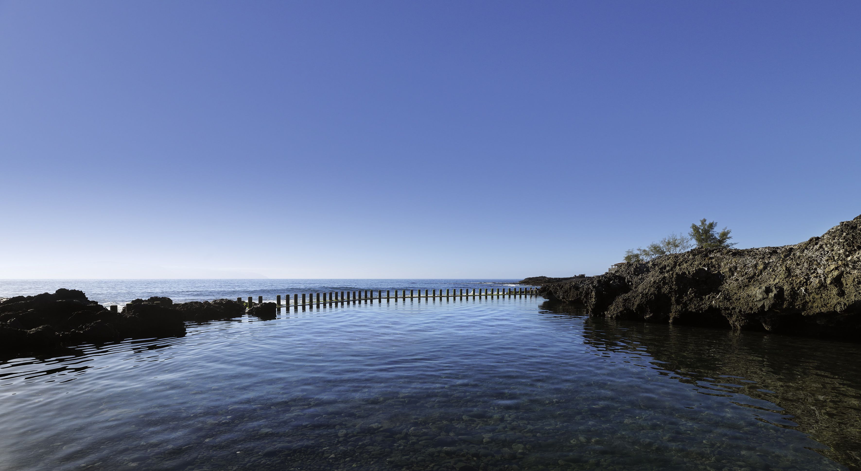 A clear view of a coastal area with calm waters, a wooden pier, and rocky terrain.