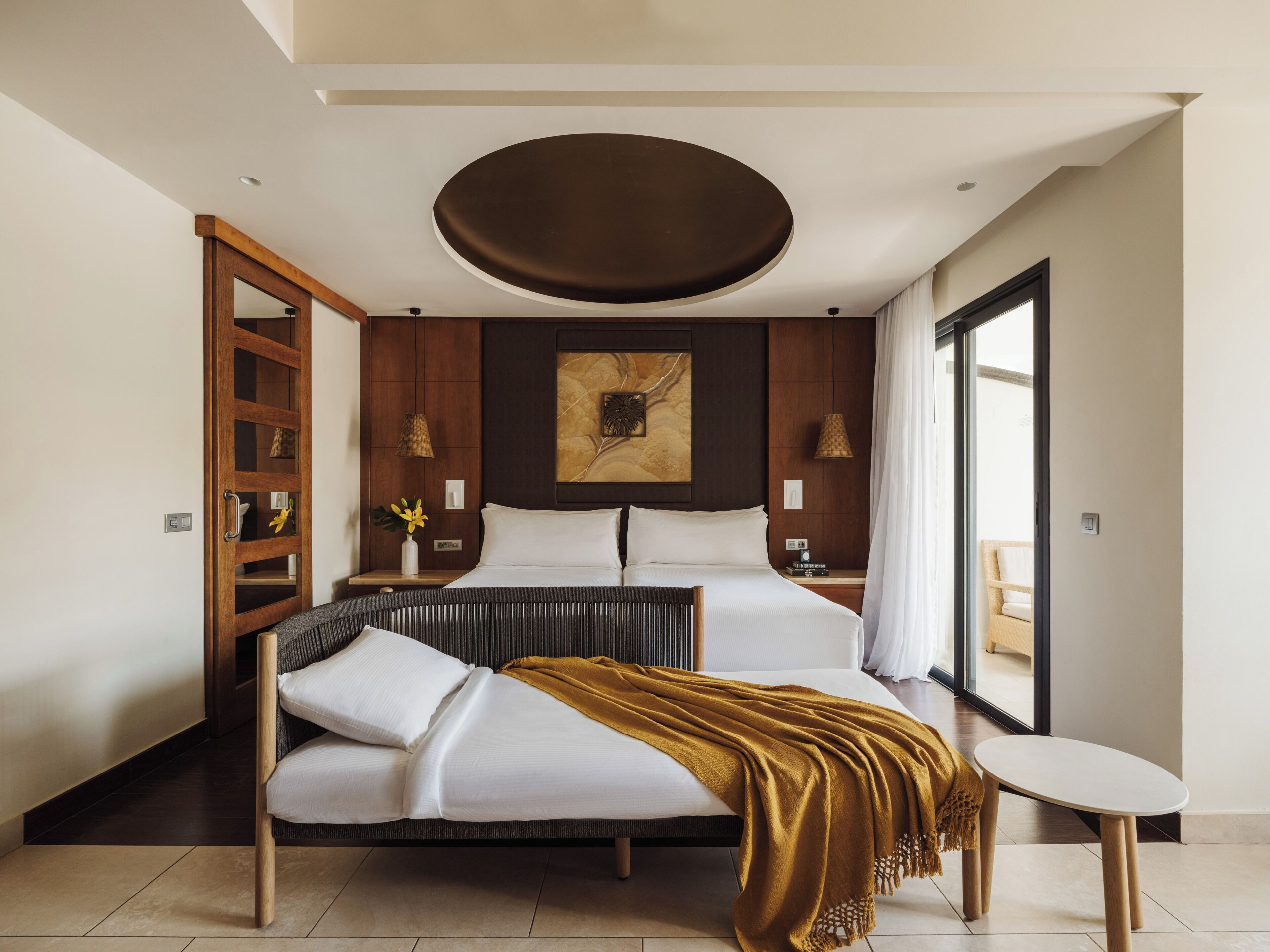 Un dormitorio moderno con una cama grande, una mesita de noche, una pequeña mesa redonda y un amplio ventanal con cortinas.