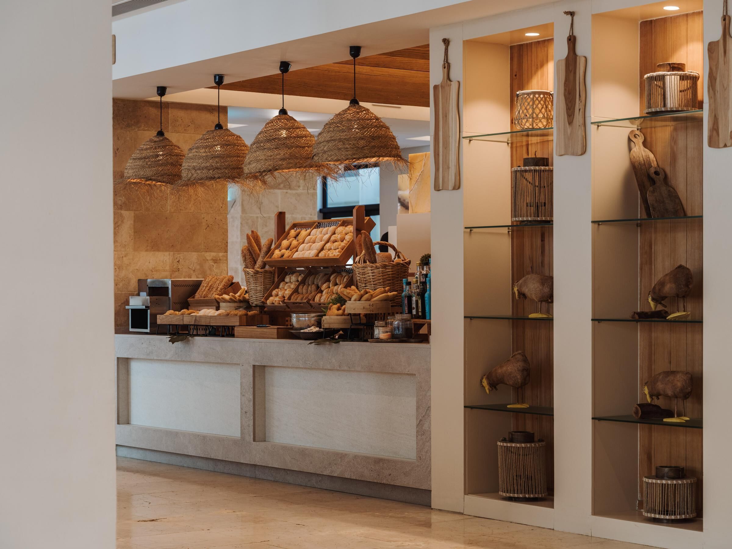 A bakery counter with bread and pastries, hanging woven light fixtures, and wooden wall decor.