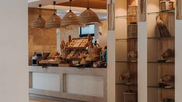 A bakery counter with bread and pastries, hanging woven light fixtures, and wooden wall decor.