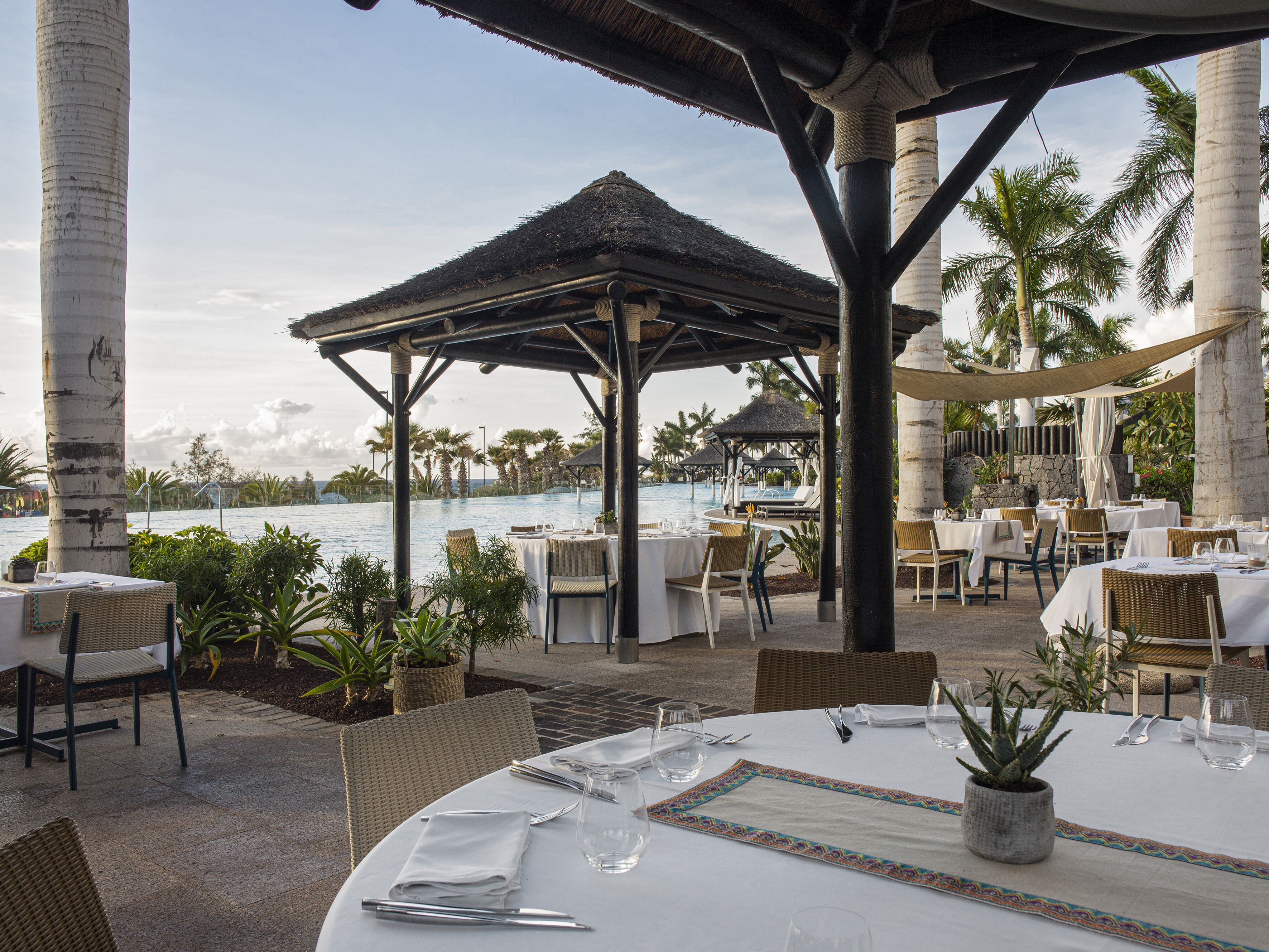 A resort patio with tables set for dining, overlooking a pool area with lounge chairs and umbrellas.