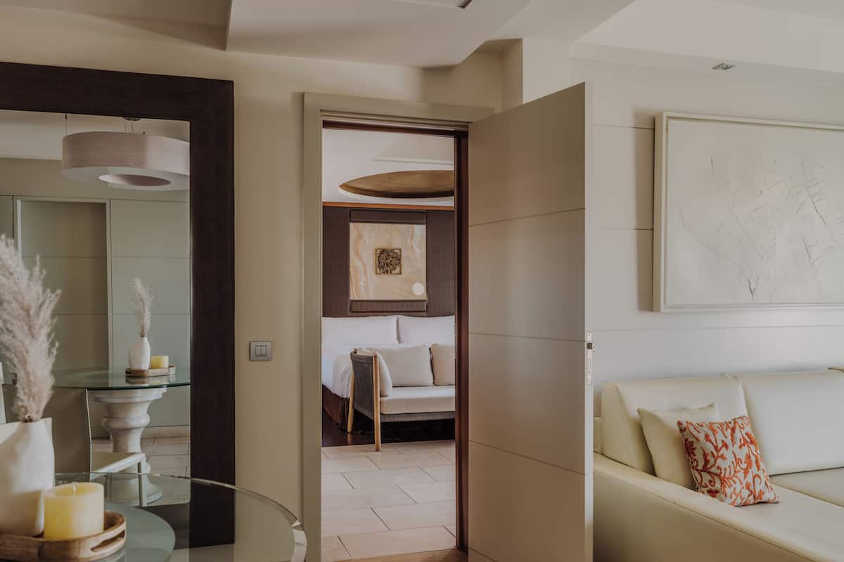 Une chambre d’hôtel moderne avec une table en verre, un canapé, un lit et une œuvre d’art accrochée au mur.