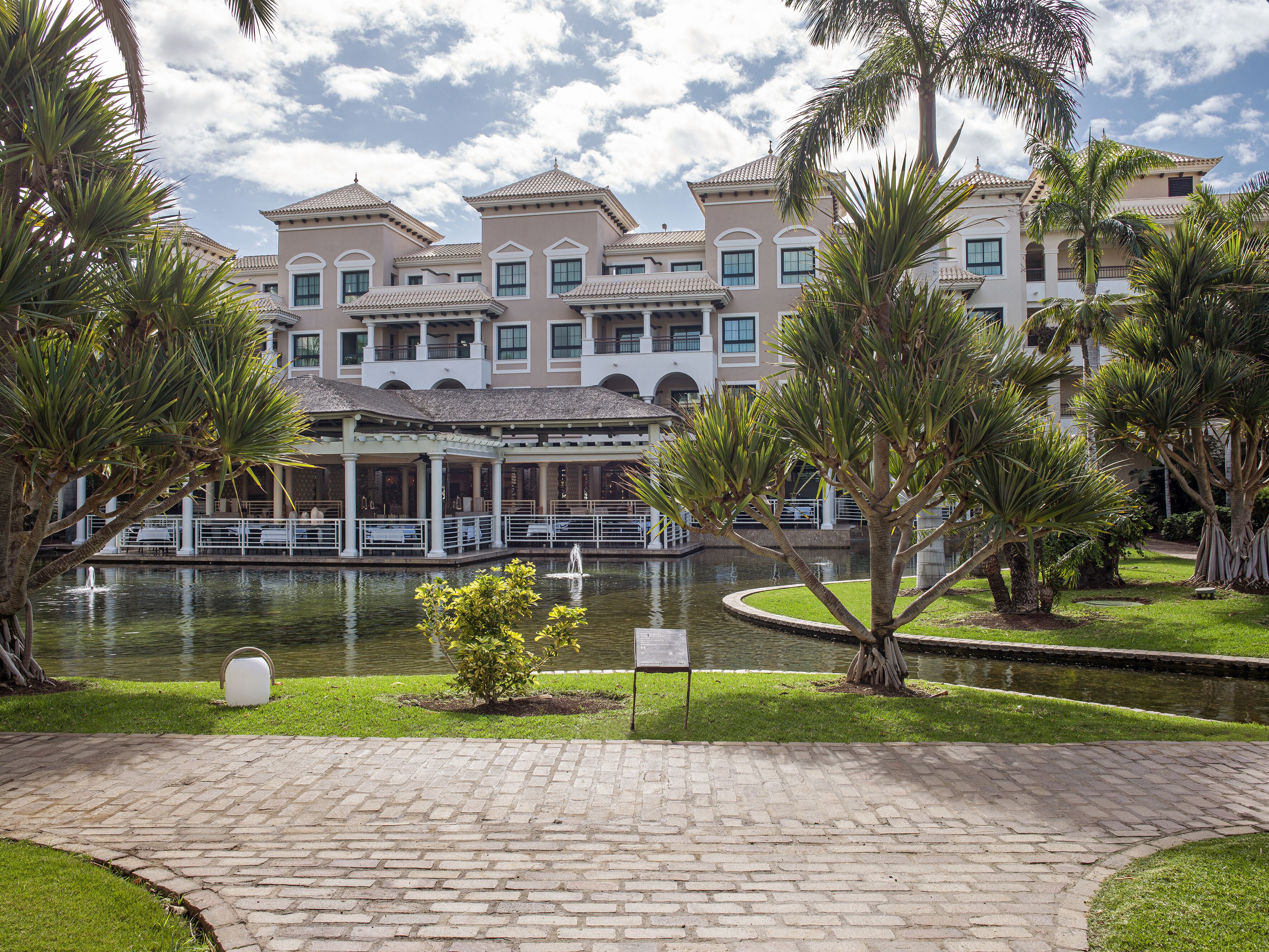 A hotel with a courtyard featuring a fountain, palm trees, and a brick pathway.