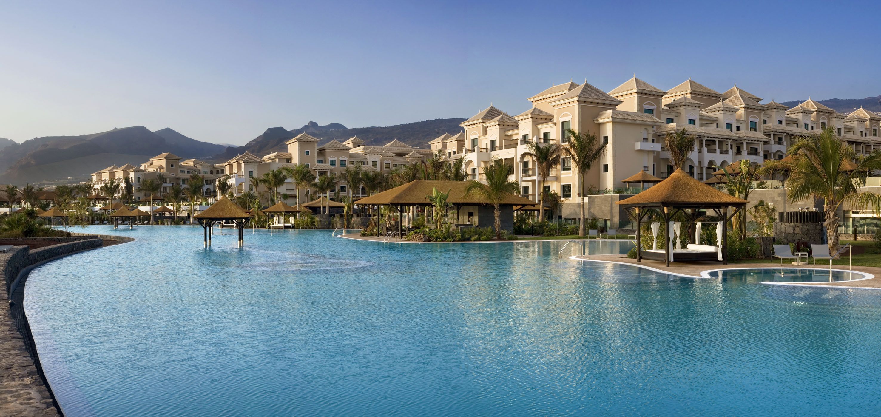Un resort con una amplia piscina, varias edificaciones con balcones y palmeras.