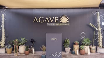 Een bord voor AGAVE POOL MEXICAN RESTAURANT, met een modern ontwerp en diverse potplanten eromheen.