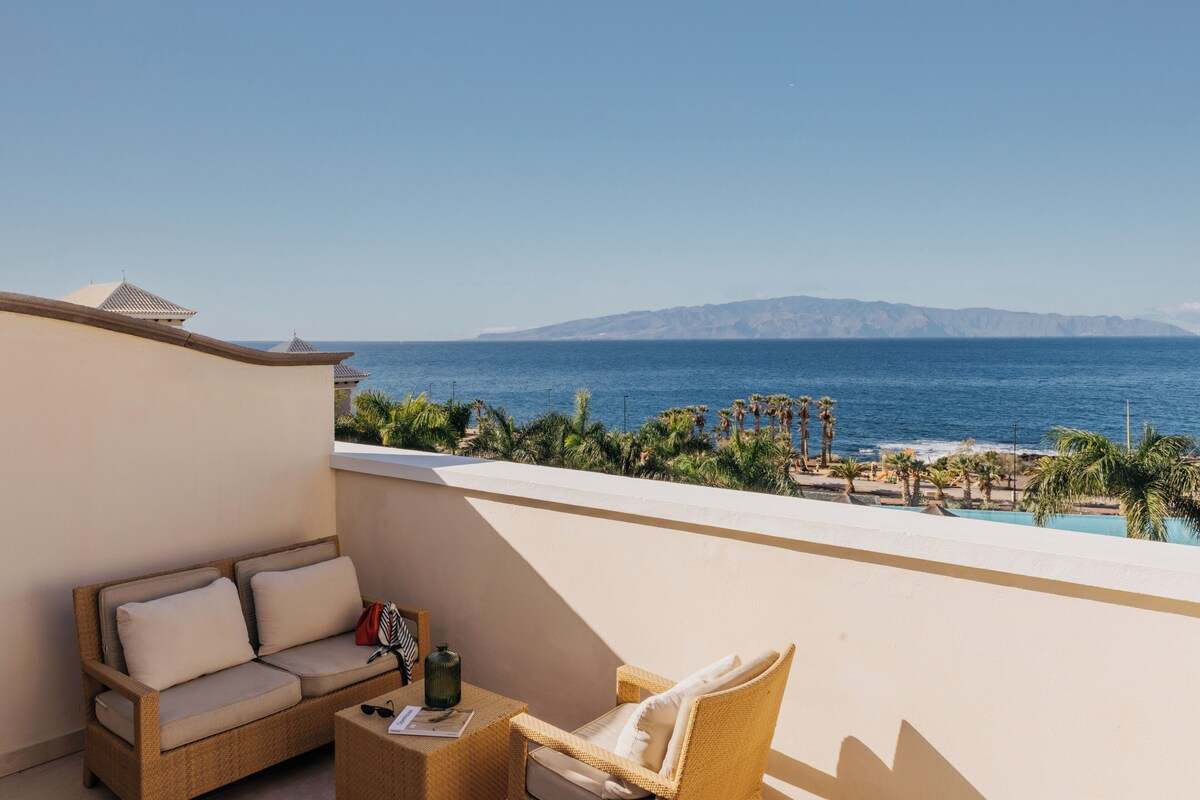 Un balcón con sofá y sillón de mimbre, con vistas a la playa y el océano.
