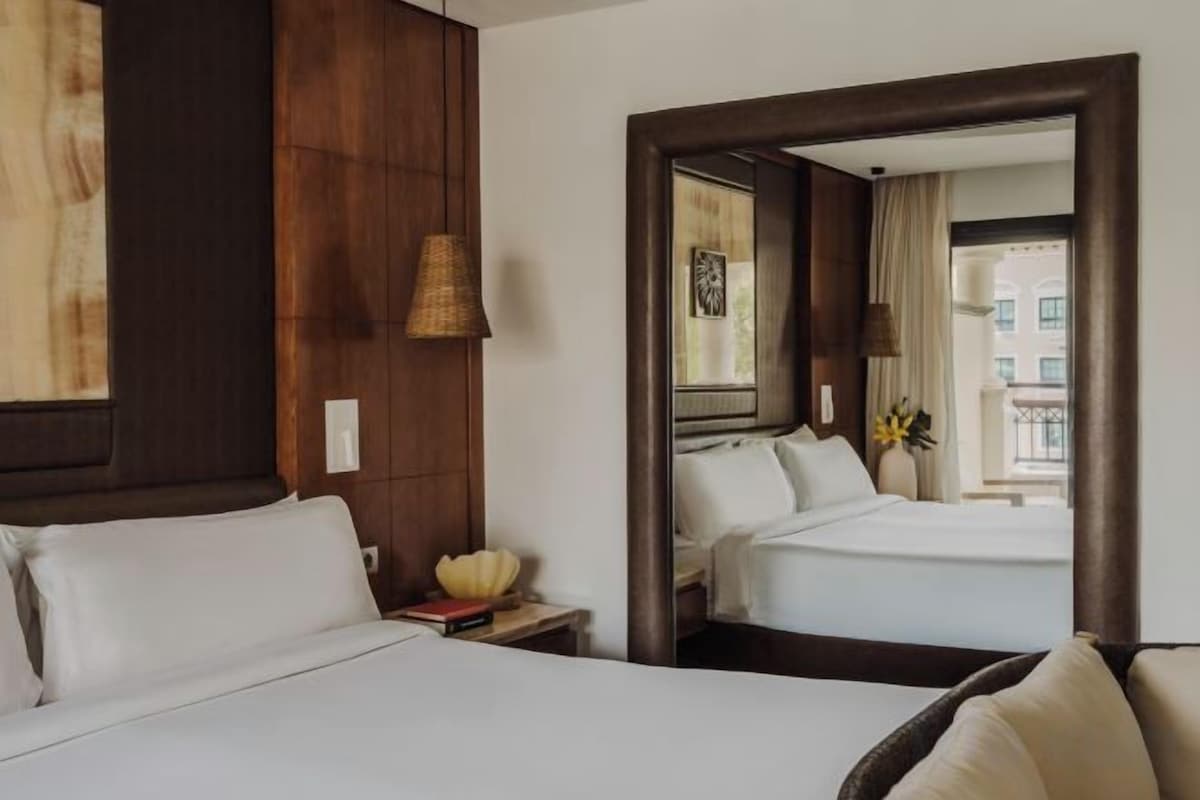 Een hotelkamer met twee bedden, een accentmuur van hout, een spiegel die de kamer weerspiegelt en uitzicht op buiten.
