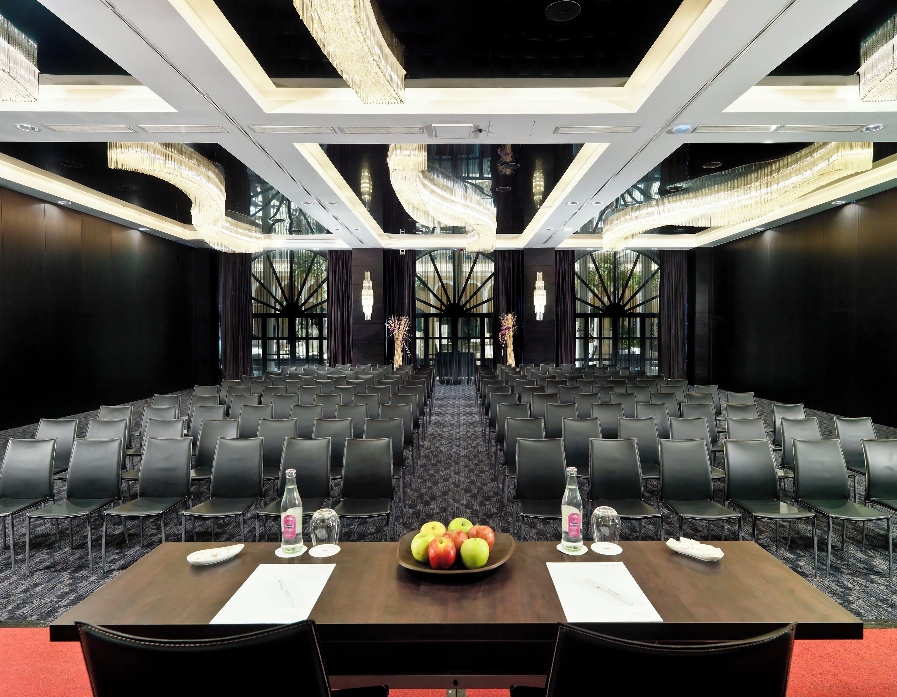 A conference room with rows of chairs, a table with a fruit bowl, water bottles, and documents.