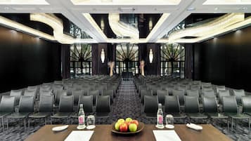 A conference room with rows of chairs, a table with a fruit bowl, water bottles, and documents.