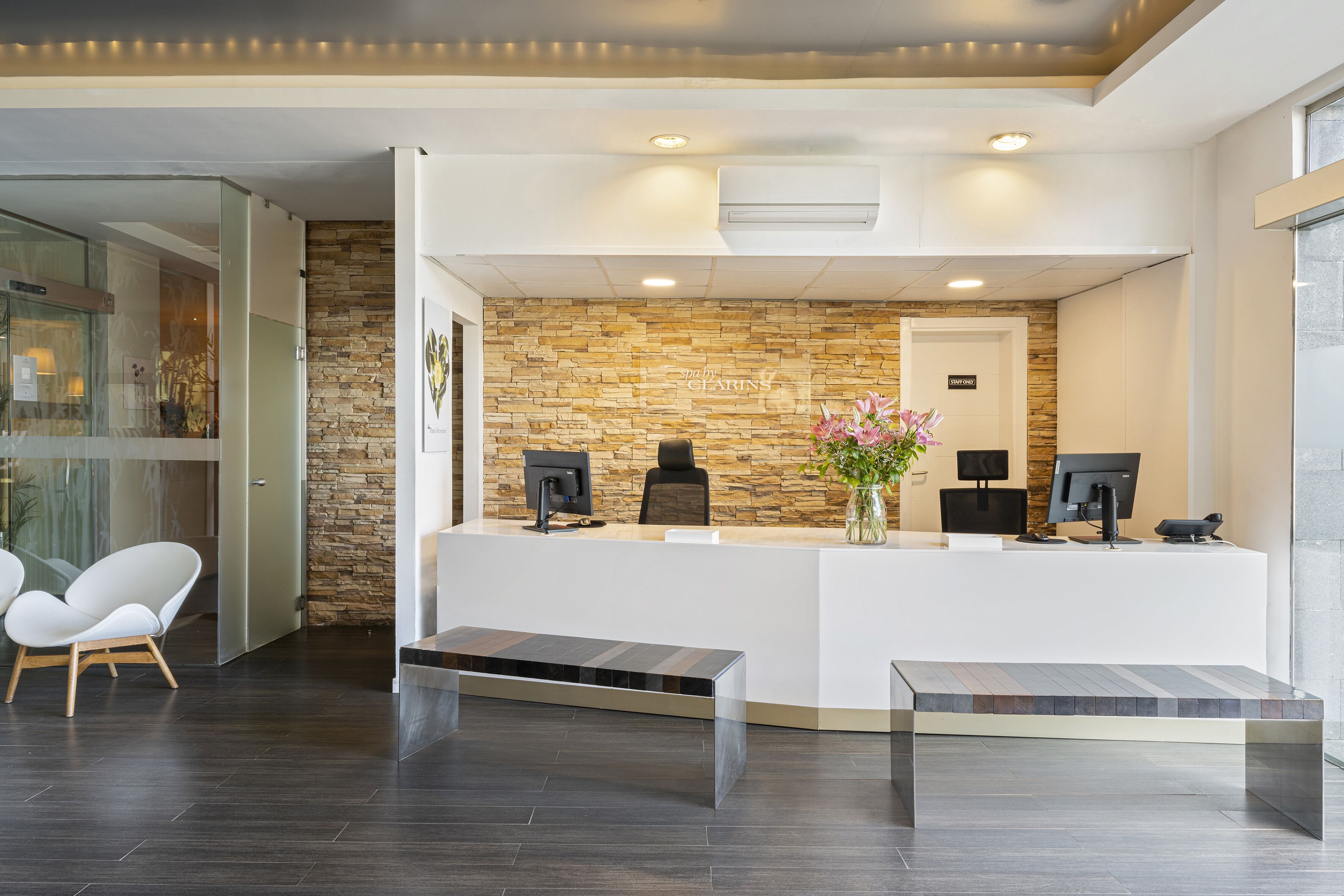 Una zona de recepción con pared de piedra, dos monitores de computadora, un mostrador de recepción y un banco.