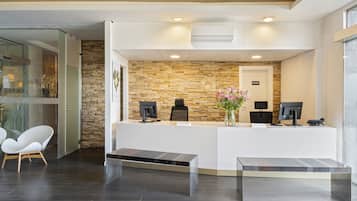 Una zona de recepción con pared de piedra, dos monitores de computadora, un mostrador de recepción y un banco.