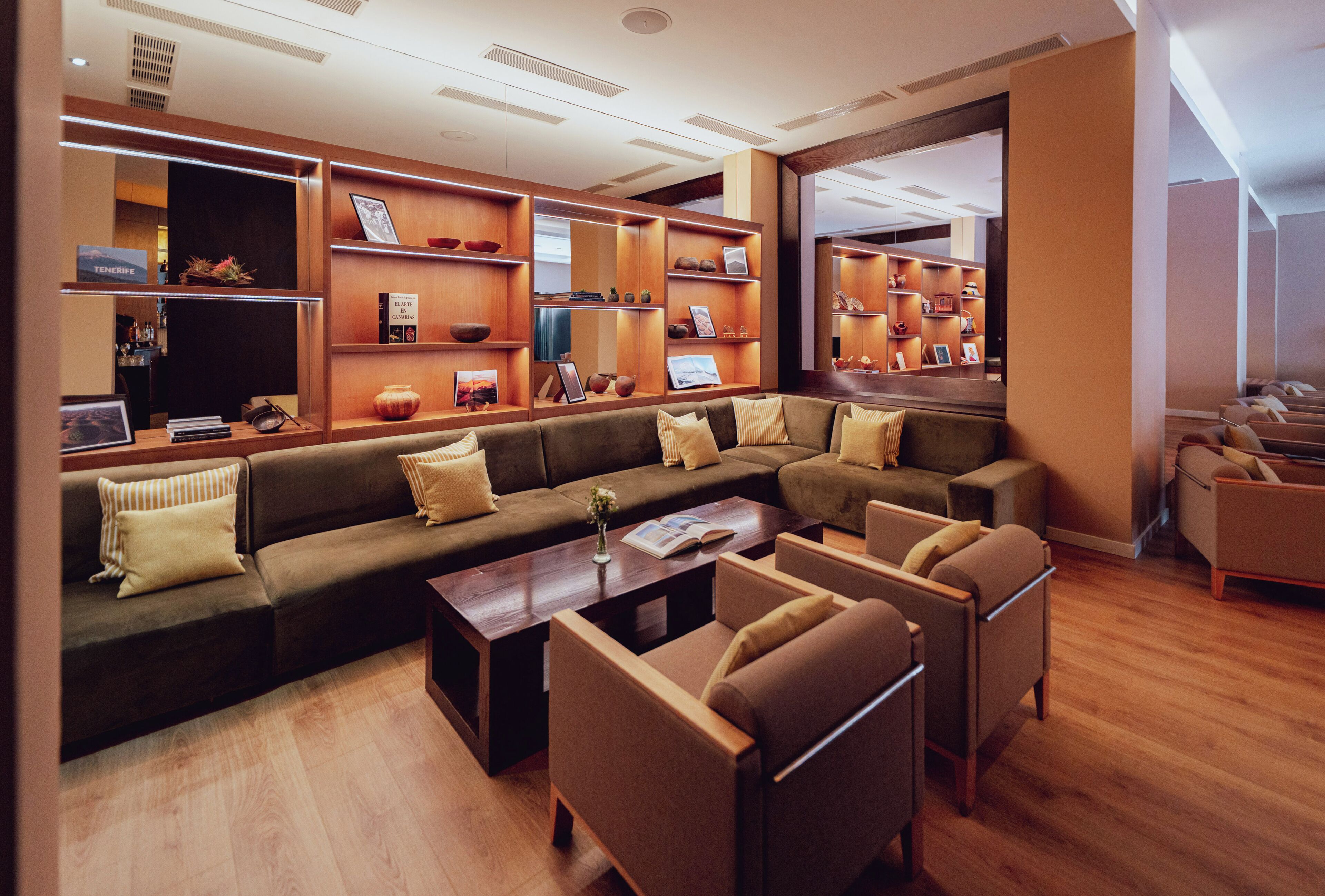 Un hall d'hotel modern amb un sofà modular, butaques, una taula de centre i prestatgeries de fusta amb diversos objectes.