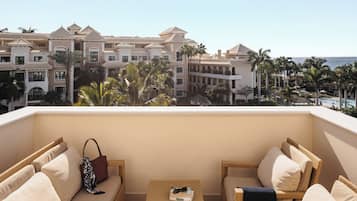 Un balcón con mobiliario de mimbre, una mesita y vistas a un edificio de resort con palmeras.