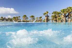 Una piscina con agua cristalina azul, rodeada de palmeras y un pabellón.