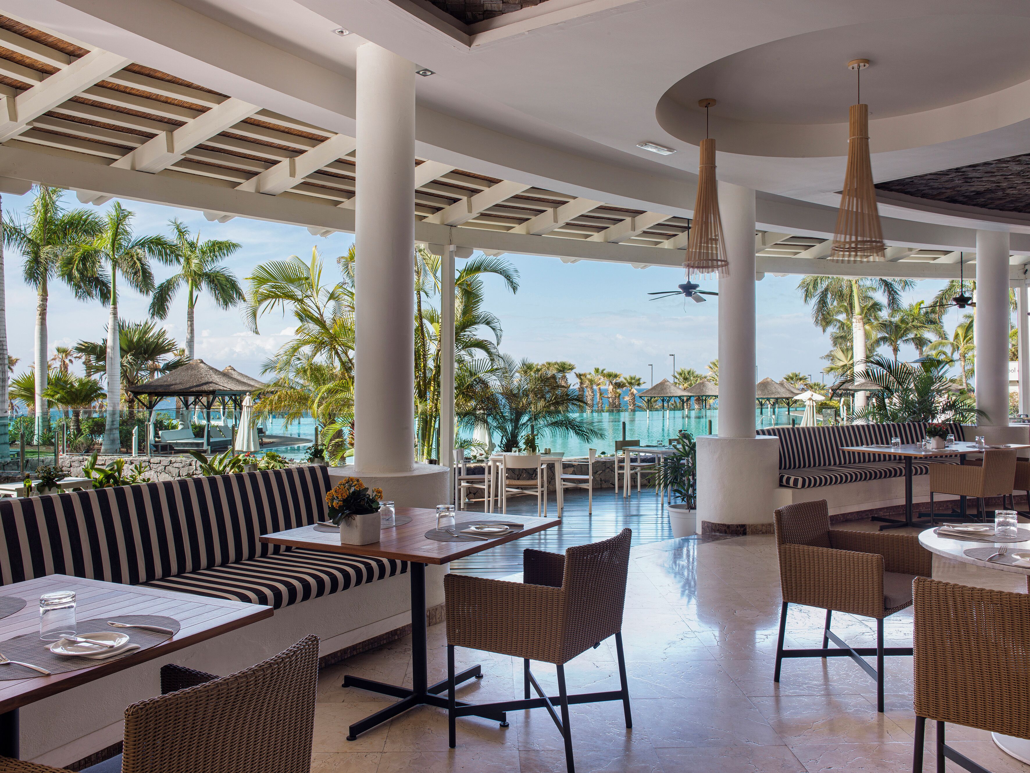 Zona de comedor al aire libre en un resort, con vista a la piscina, con mesas y asientos.