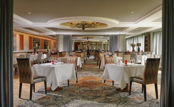 Un comedor formal con mesas dispuestas para el servicio, un candelabro y piso alfombrado.