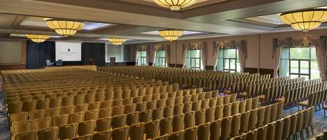 Un salón de conferencias con filas de sillas, un atril y una pantalla de presentación.