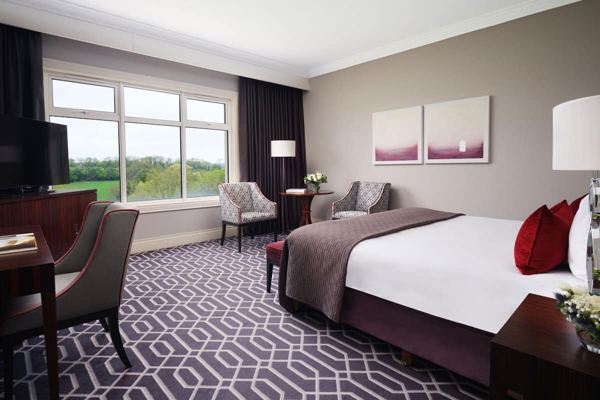 Ein Hotelzimmer mit einem großen Bett, zwei Sesseln, einem Schreibtisch mit Fernseher, einer Lampe und Bildern an der Wand.
