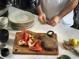 A chef preparing a dish with lobster, steak, and lemon on a wooden board.