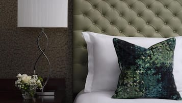A bedroom with a tufted headboard, a white pillow, a decorative pillow, a bedside table with a vase of flowers, and a wall-mounted lamp.