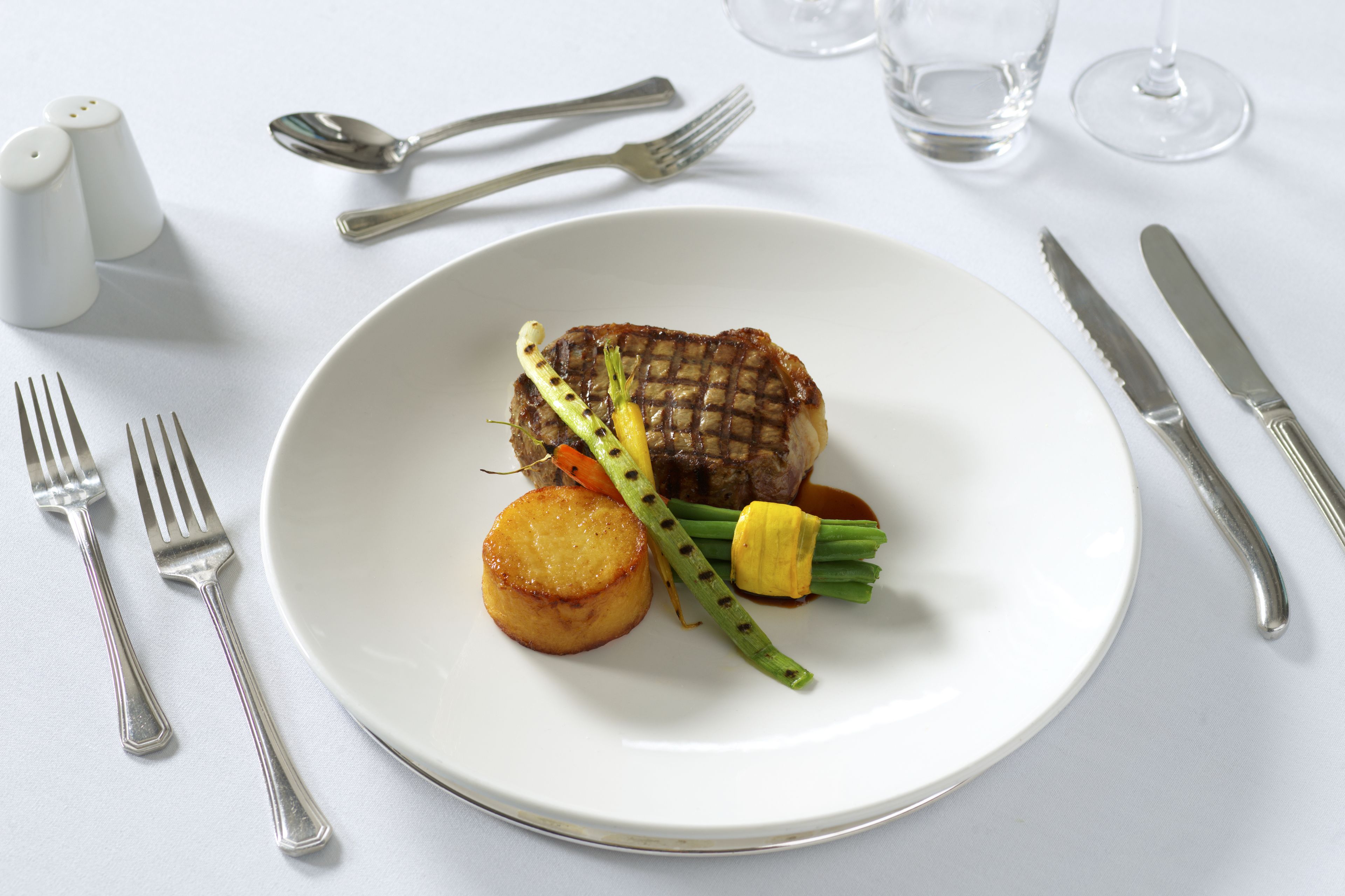 A plate with a grilled steak, a roasted potato, and grilled asparagus on a white table.