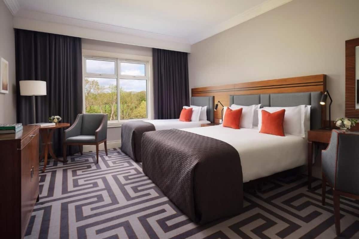 Ein Hotelzimmer mit zwei Betten, einem Schreibtisch, einem Stuhl und einem fensterbelagten Fenster.