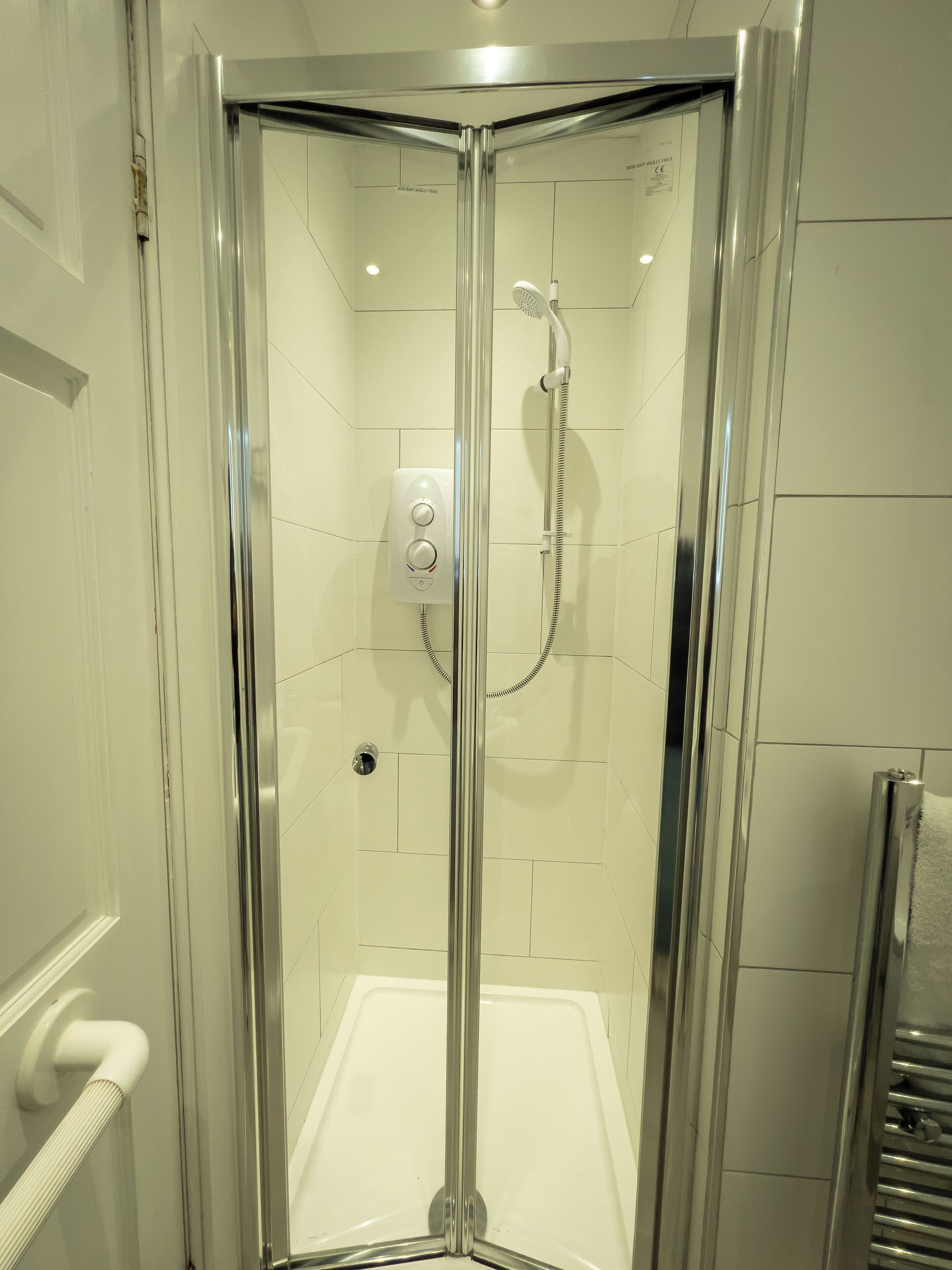 A corner shower with a glass door, a handheld showerhead, and a control panel.