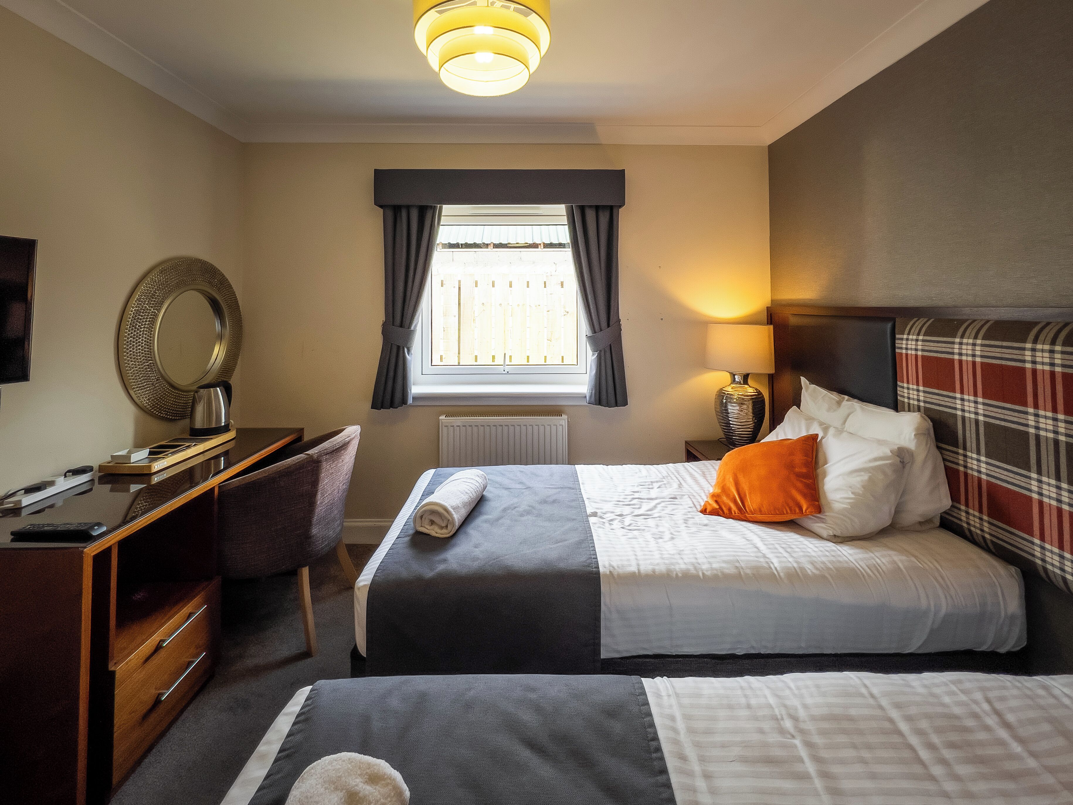 A hotel room with two beds, a desk, a chair, a television, a window with curtains, and a lamp.