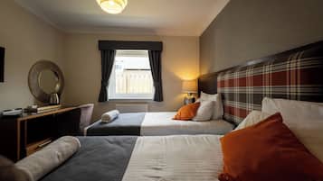 A hotel room with two beds, a large mirror, a window with curtains, and a headboard with a plaid pattern.