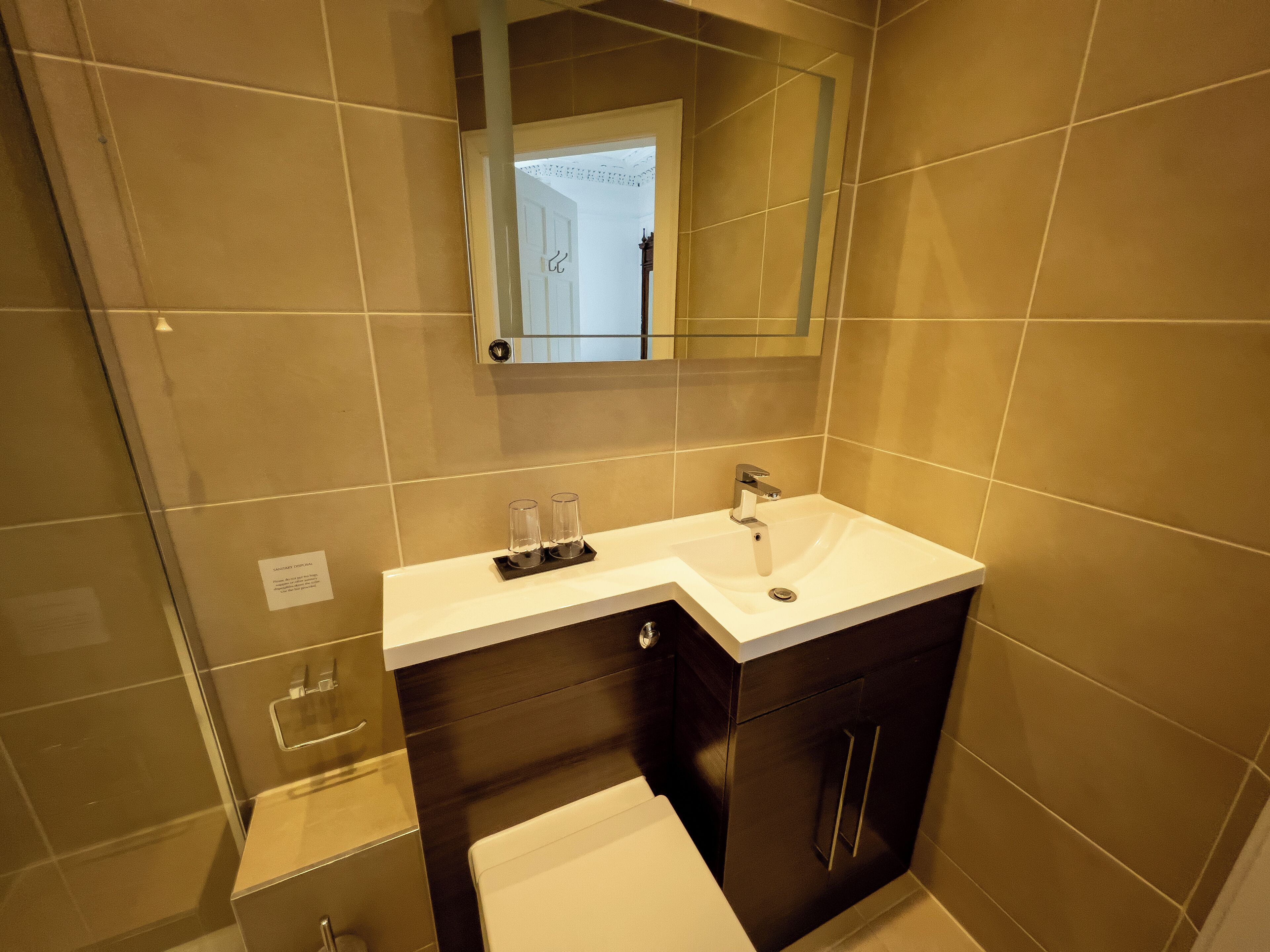 Une salle de bain moderne avec un lavabo blanc, des meubles en bois foncé et un miroir au-dessus du lavabo.
