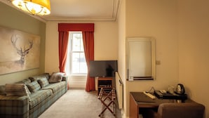 Ett mysigt vardagsrum med en soffa, en tv, ett skrivbord med en stol och ett fönster med gardiner.