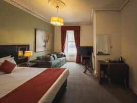 A hotel room with a bed, a sofa, a desk, a television, and a painting of a deer.