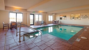 Una piscina interior con una estación de salvavidas, sillas y una sala iluminada con vistas.