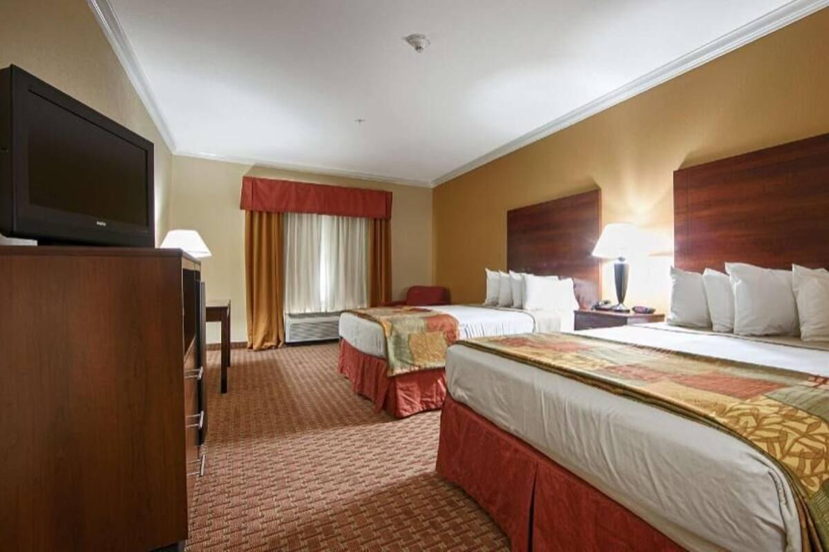 A hotel room with two beds, a television, a desk, and a window with curtains.