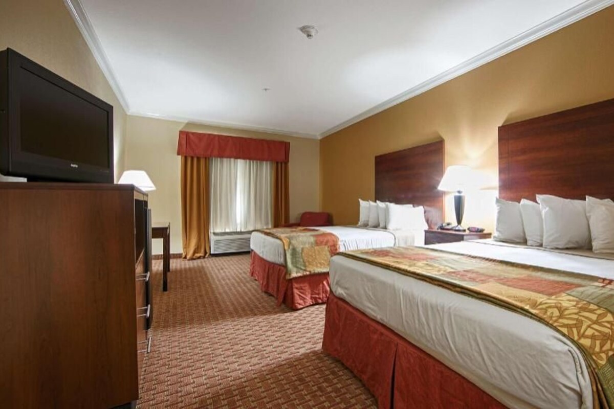 Habitación de hotel con dos camas, televisión, escritorio y ventana con cortinas.