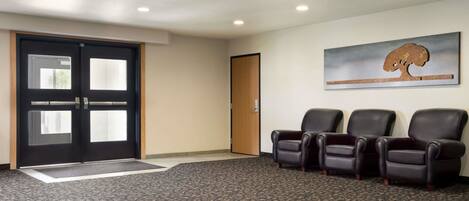 A waiting area with a carpeted floor, a door with a glass panel, and three leather chairs.
