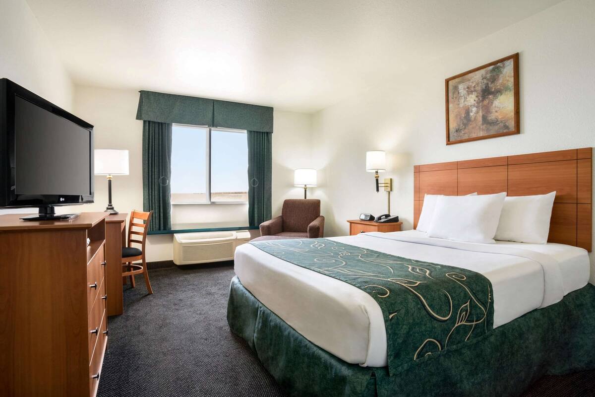 Ein Hotelzimmer mit Bett, Schreibtisch, Stuhl, Fernseher und einem Fenster mit Vorhängen.