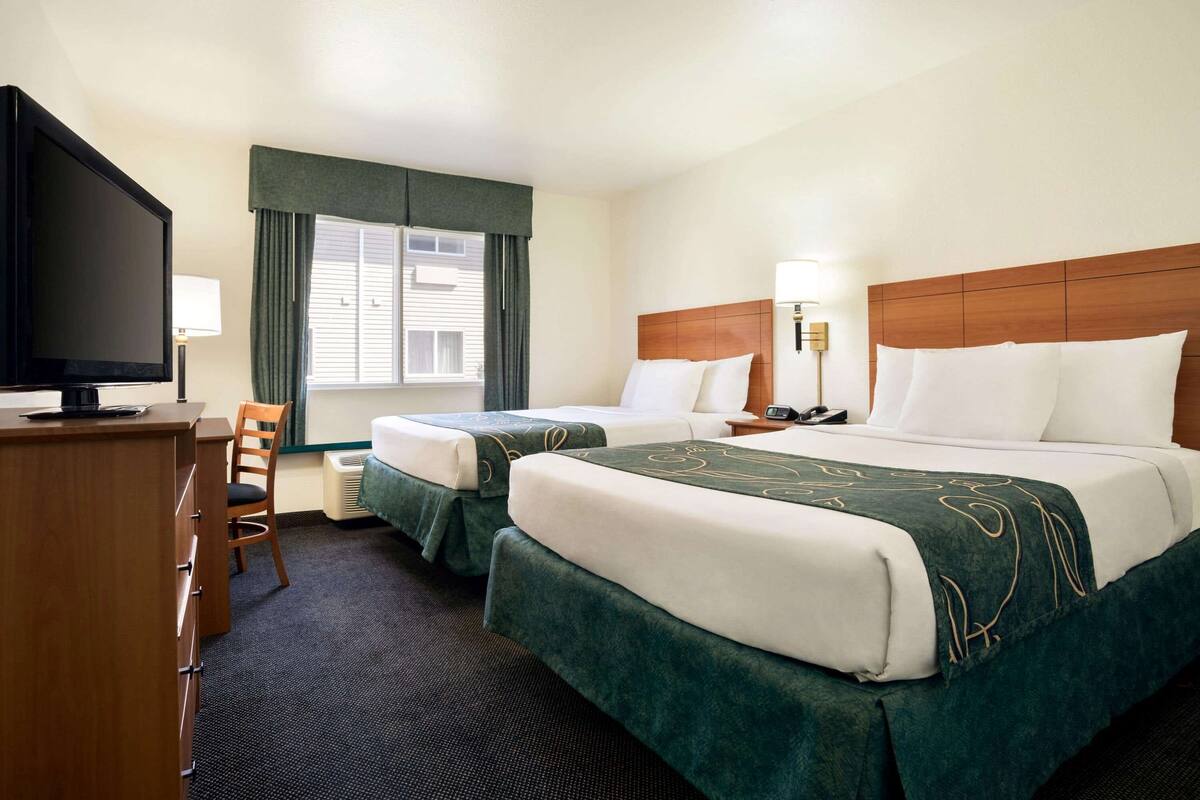 Ein Hotelzimmer mit zwei Betten, einem Schreibtisch, einem Fernseher und einem Fenster mit Vorhängen.