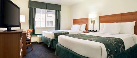 A hotel room with two beds, a desk, a television, and a window with curtains.