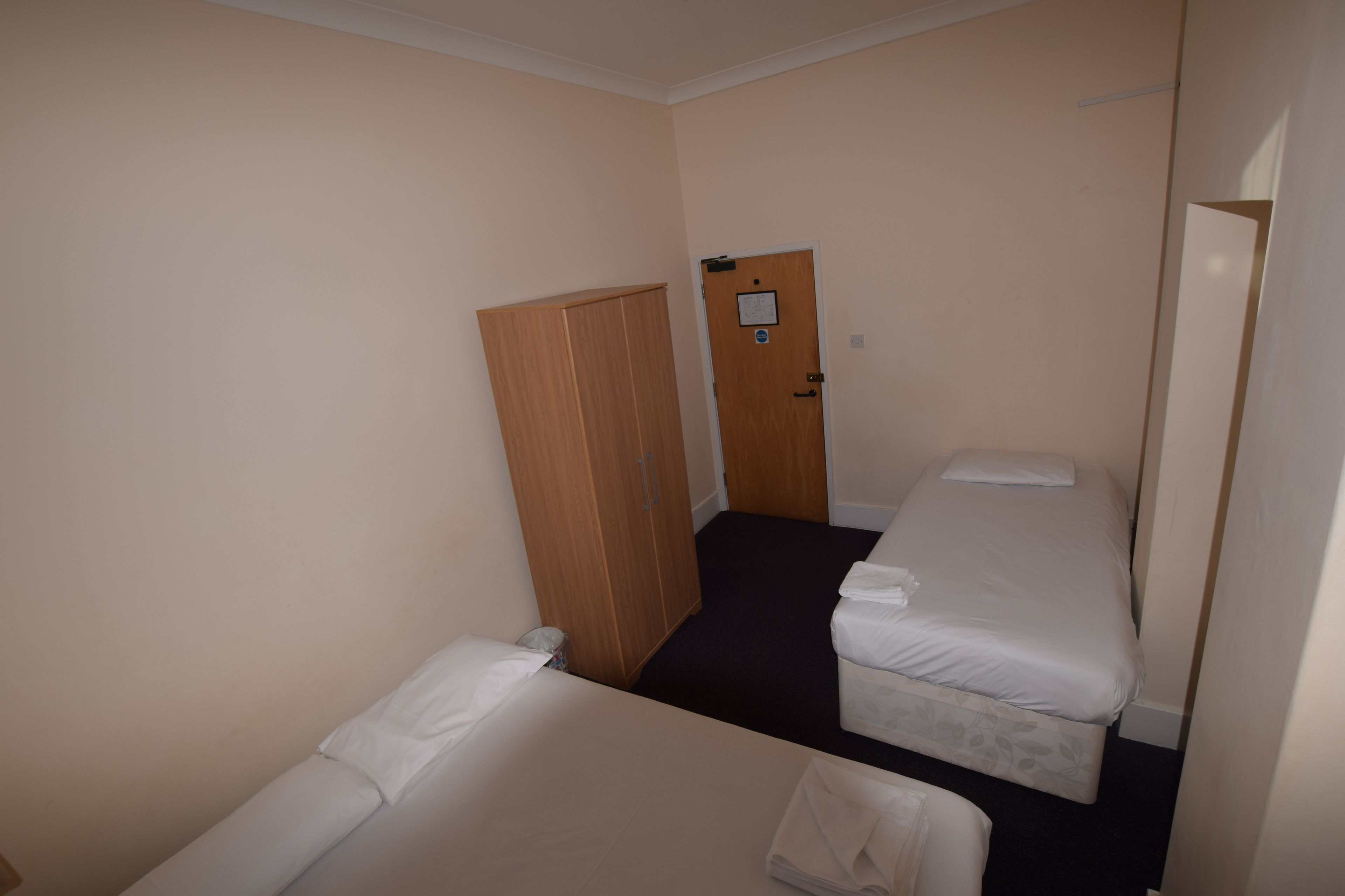 Habitación de hotel con dos camas individuales, un armario de madera y una puerta con un aviso.