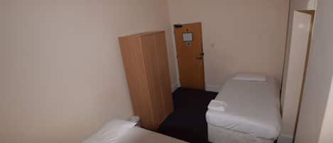Habitación de hotel con dos camas individuales, un armario de madera y una puerta con un aviso.