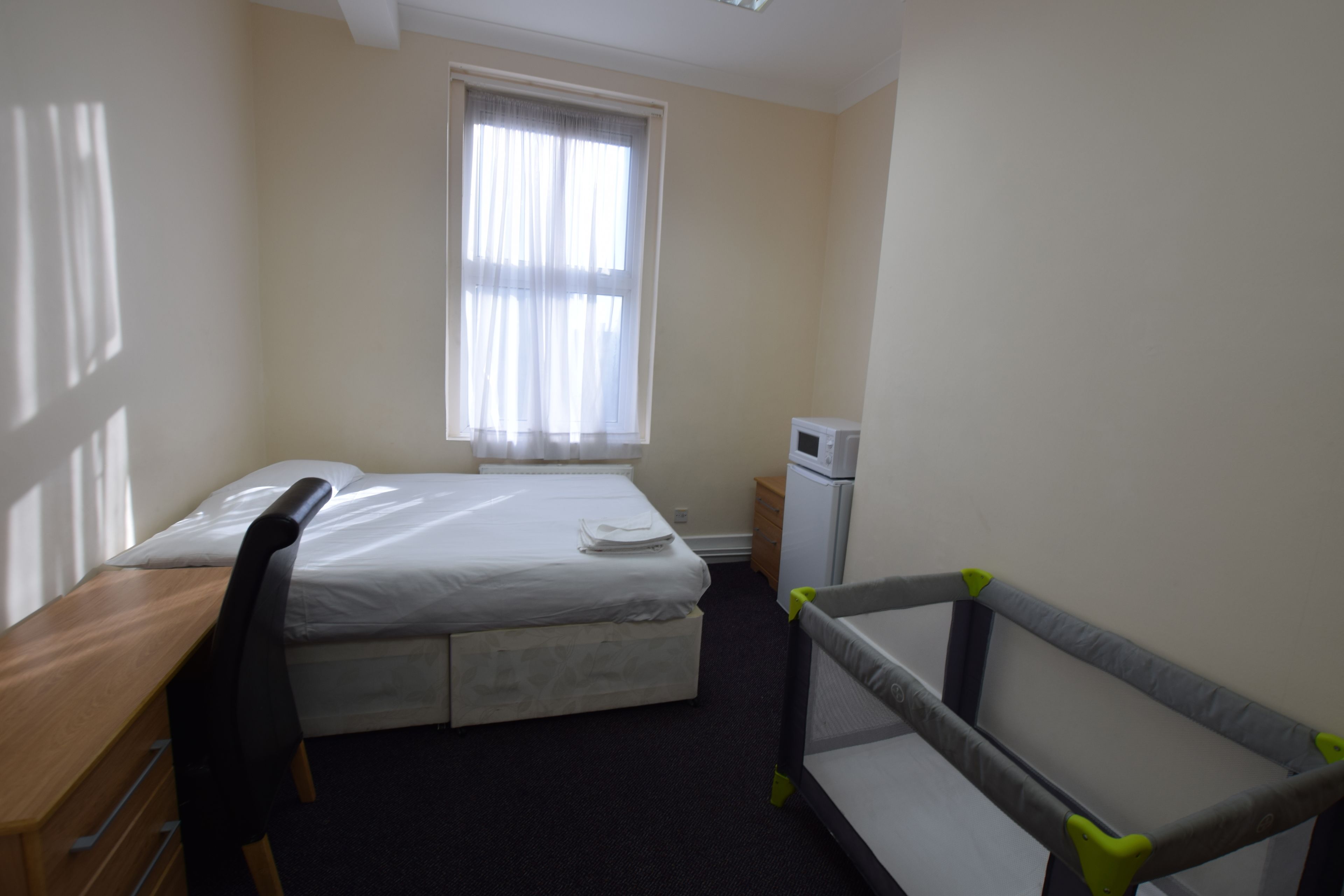 A hotel room with a bed, a desk, a chair, a crib, and a small refrigerator.