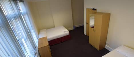 Una habitación de hotel con una cama individual, un armario de madera, un escritorio y una ventana con persianas.