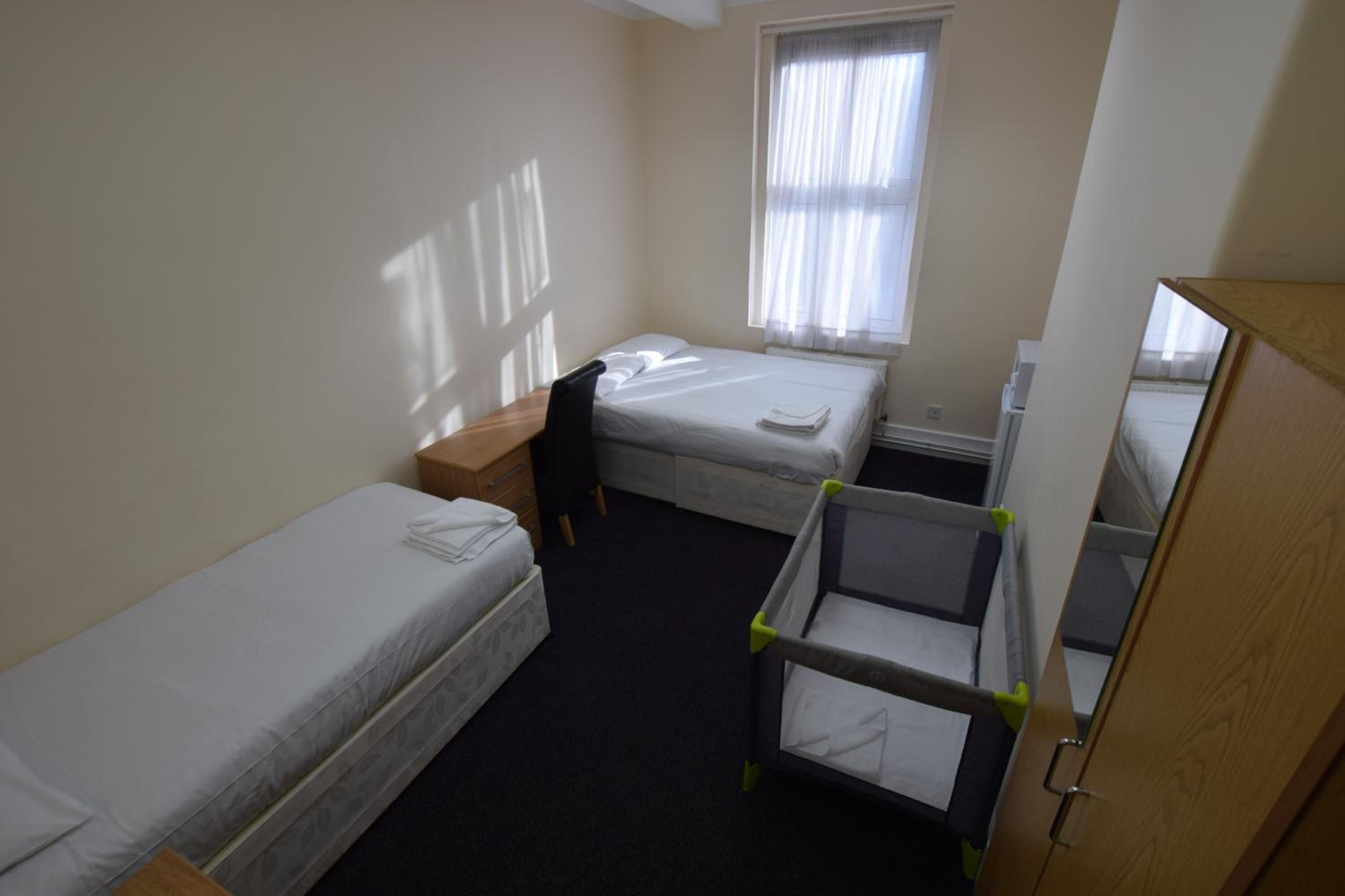 A small, clean room with two single beds, a desk, a chair, and a crib.